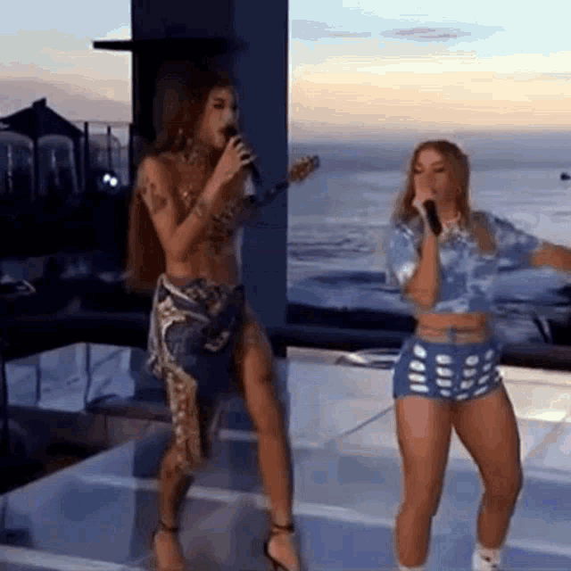 a woman is singing into a microphone while another woman stands next to her on a stage .