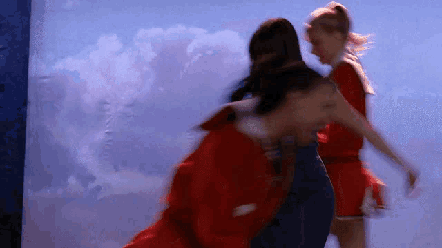 a group of cheerleaders are dancing in front of a blue sky with clouds