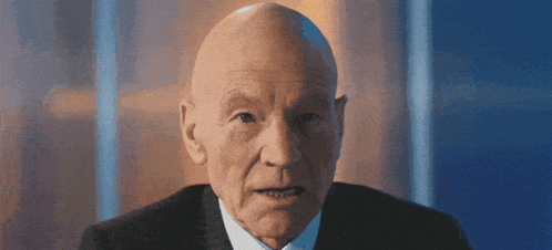 a bald man wearing a suit and tie is looking at the camera .