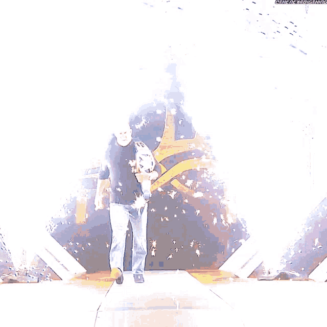 a man in a blue shirt is walking down a stage holding a wrestling championship belt