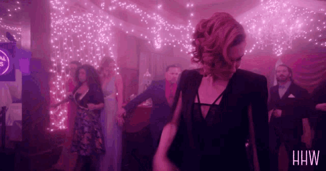 a woman in a black dress is dancing in a room with a sign that says hw