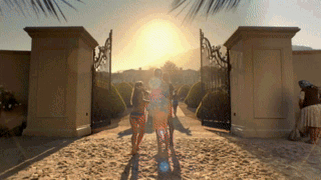a group of people walking through a gate with the sun in the background