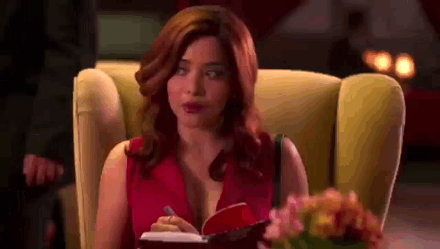 a woman in a red dress is sitting in a yellow chair writing in a red notebook .