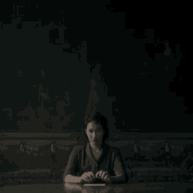 a woman sits at a table with her hands folded in front of a painting