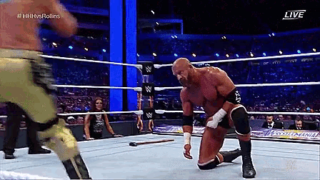 a wrestler is kneeling down in a wrestling ring while another wrestler kicks him .