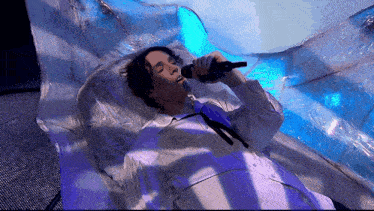 a man singing into a microphone while laying in a bed