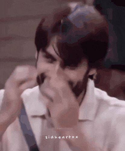 a man in a white shirt is covering his mouth with his hand and the words sidheartxxx are on the bottom of the image