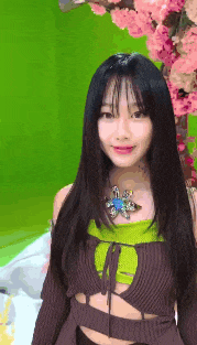 a woman with long black hair is standing in front of a green screen with pink flowers in the background .