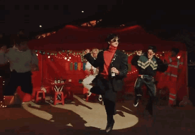 a group of people are dancing in a room with a red wall behind them .