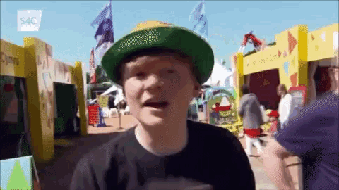 a man wearing a green hat and a black shirt stands in front of a yellow building that says 54c