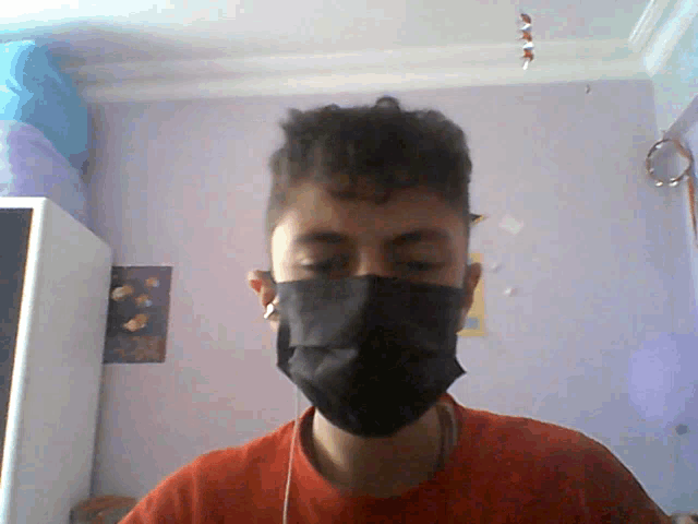 a man wearing a black mask and ear buds looks at the camera