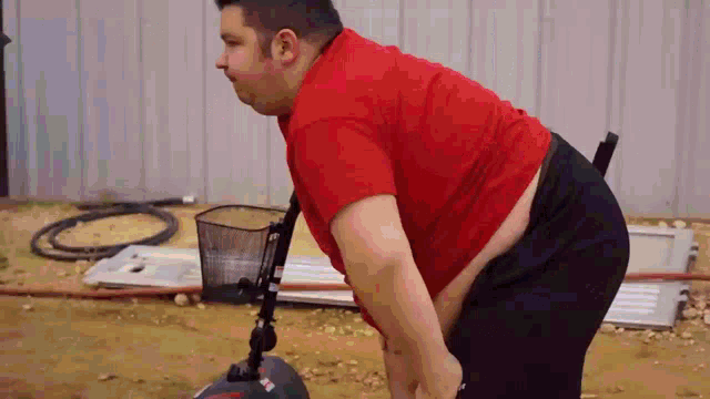 a man in a red shirt is using a vacuum cleaner to clean the ground