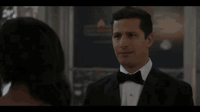 a man in a tuxedo looks at a woman in a dress