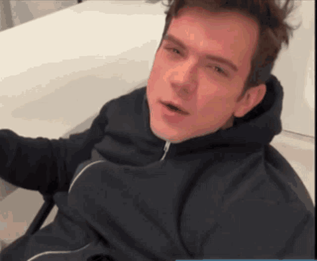 a young man in a black hoodie is laying on a white surface