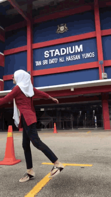 a woman is standing in front of a stadium that says tan sri dato hj hassan yunos