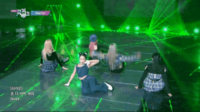 a woman in a blue tank top is kneeling down on a stage in front of green lights