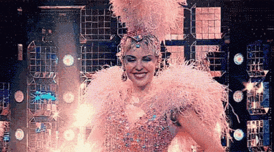 a woman is wearing a pink feathered costume and a crown on a stage .