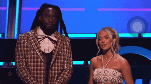 a man in a plaid jacket stands next to a woman in a white crop top
