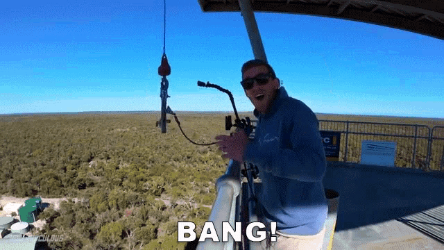 a man in a blue sweatshirt stands in front of a microphone with the word bang above him