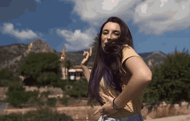 a woman with purple hair is standing in front of a mountain