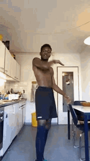 a shirtless man is dancing in a kitchen while wearing shorts and socks .