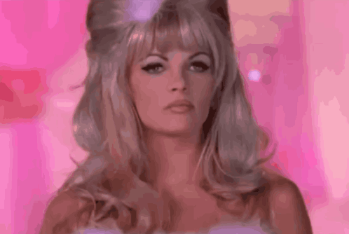 a woman with blonde hair and a pink background is wearing a wig .