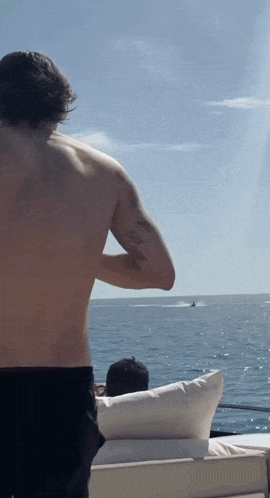 a shirtless man is standing on a boat in the ocean looking at a boat .
