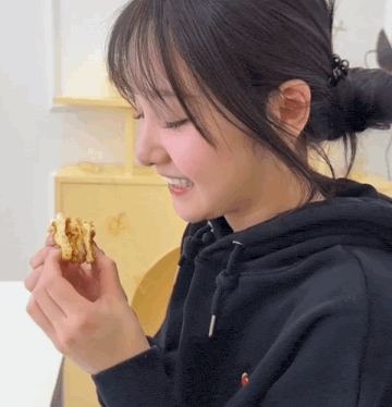 a woman wearing a black hoodie is eating a piece of cake
