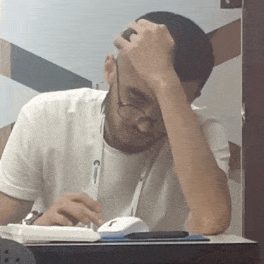 a man wearing glasses and a lanyard with the letter c on it sits at a desk