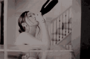 a woman is drinking wine from a bottle in a bathroom .