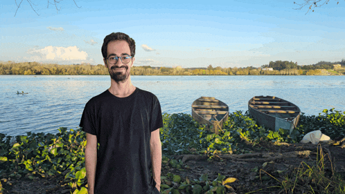 a man in a black shirt stands in front of a body of water
