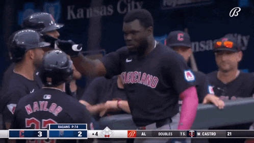 a baseball player wearing a black cleveland jersey is being congratulated by his teammates