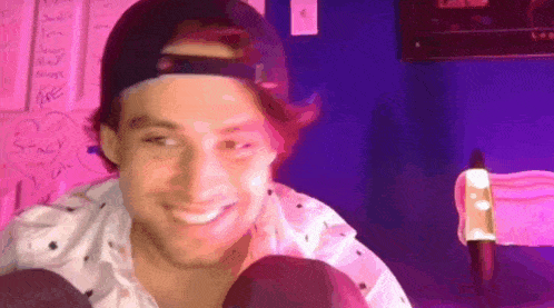 a man wearing a baseball cap and a white shirt is smiling in front of a purple wall .