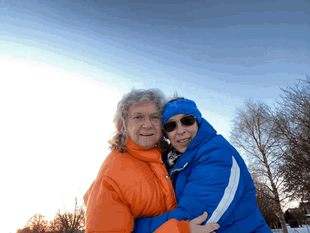 a man in an orange jacket and a woman in a blue jacket hugging