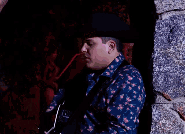 a man wearing a cowboy hat and a floral shirt is playing a guitar