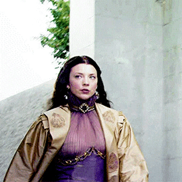 a woman wearing a purple dress and a gold jacket is walking down a sidewalk .