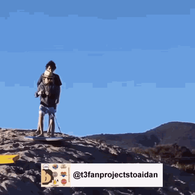 two boys standing on top of a sandy hill with a sticker that says t3fanprojecttoaidan
