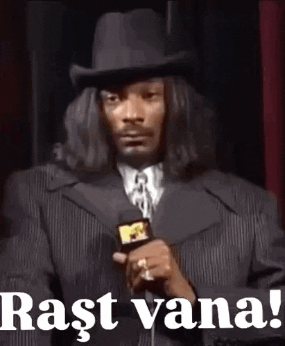 snoop dogg is wearing a suit and top hat while holding a microphone and talking into it .