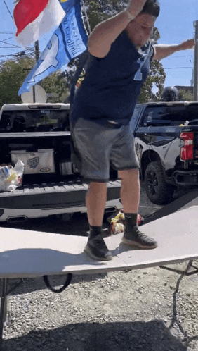 a man in a blue shirt is jumping over a table in front of a truck