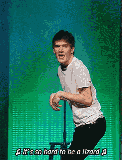 a man in a white shirt is singing it 's so hard to be a lizard in front of a green background