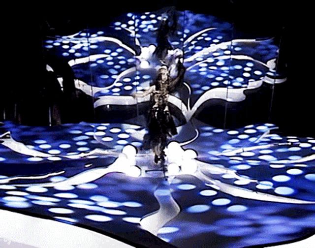 a woman is walking on a stage in front of a blue and white background