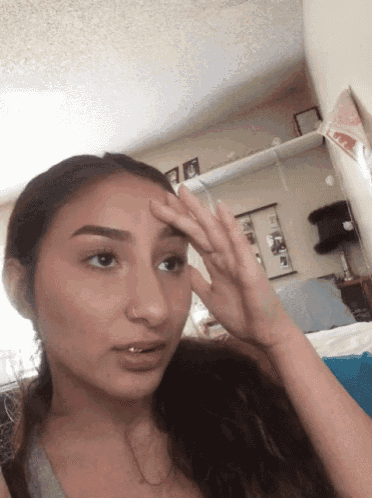 a girl with a nose ring is covering her forehead with her hand