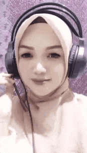 a woman wearing a hijab and headphones is smiling for the camera .