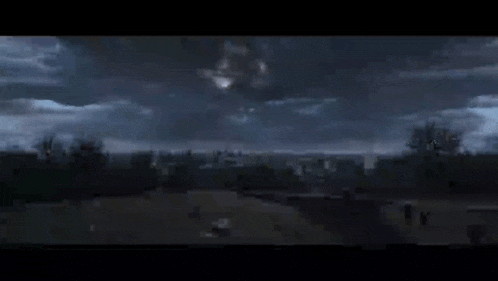 a person is standing on top of a hill looking at a group of lights flying in the night sky .