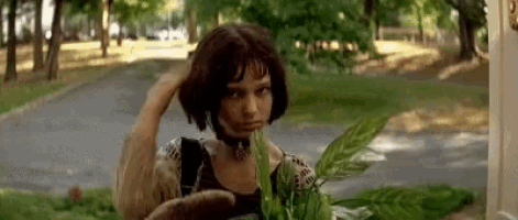 a woman is standing in front of a house holding a plant in her hands .