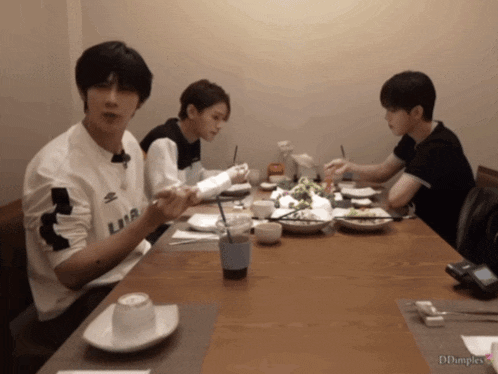 three young men are sitting at a table with one wearing a shirt that says lmr