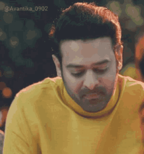 a man wearing a yellow sweater is looking down and making a funny face .