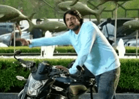 a man in a blue shirt is riding a motorcycle in front of fish sculptures