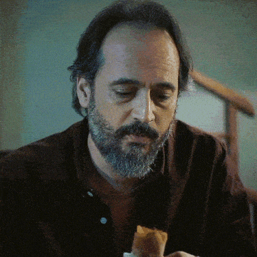 a man with a beard is sitting at a table eating a piece of food