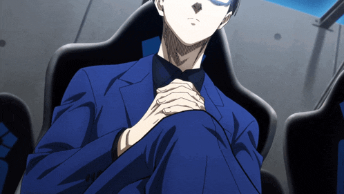 a man in a blue suit is sitting in a chair with his hands folded